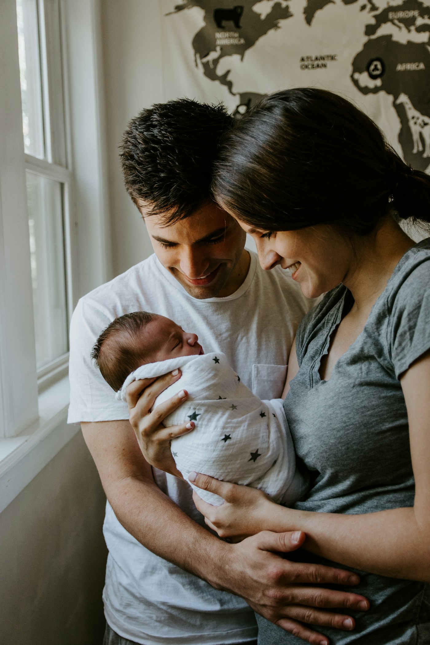 A couple looking down at their newborn baby by a window